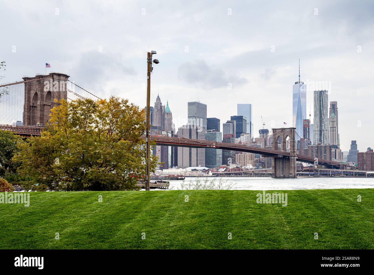 Una splendida vista mostra il Ponte di Brooklyn che collega Brooklyn e Manhattan con un parco verde in primo piano, evidenziando lo skyline. Foto Stock