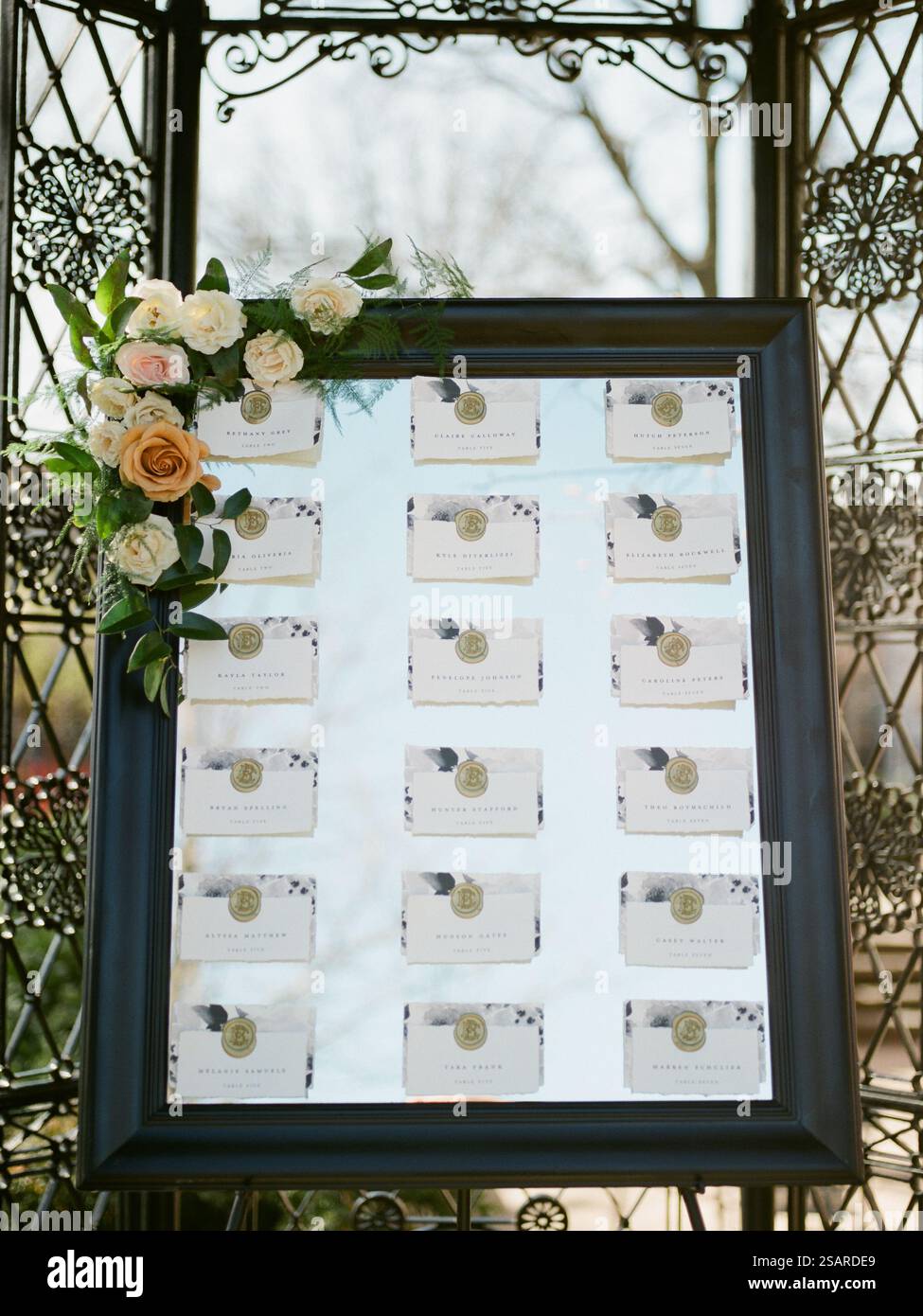 Una disposizione dei posti a sedere ben organizzata è esposta in un luogo per matrimoni all'aperto, decorato con fiori freschi e con nomi elegantemente stampati su ind Foto Stock