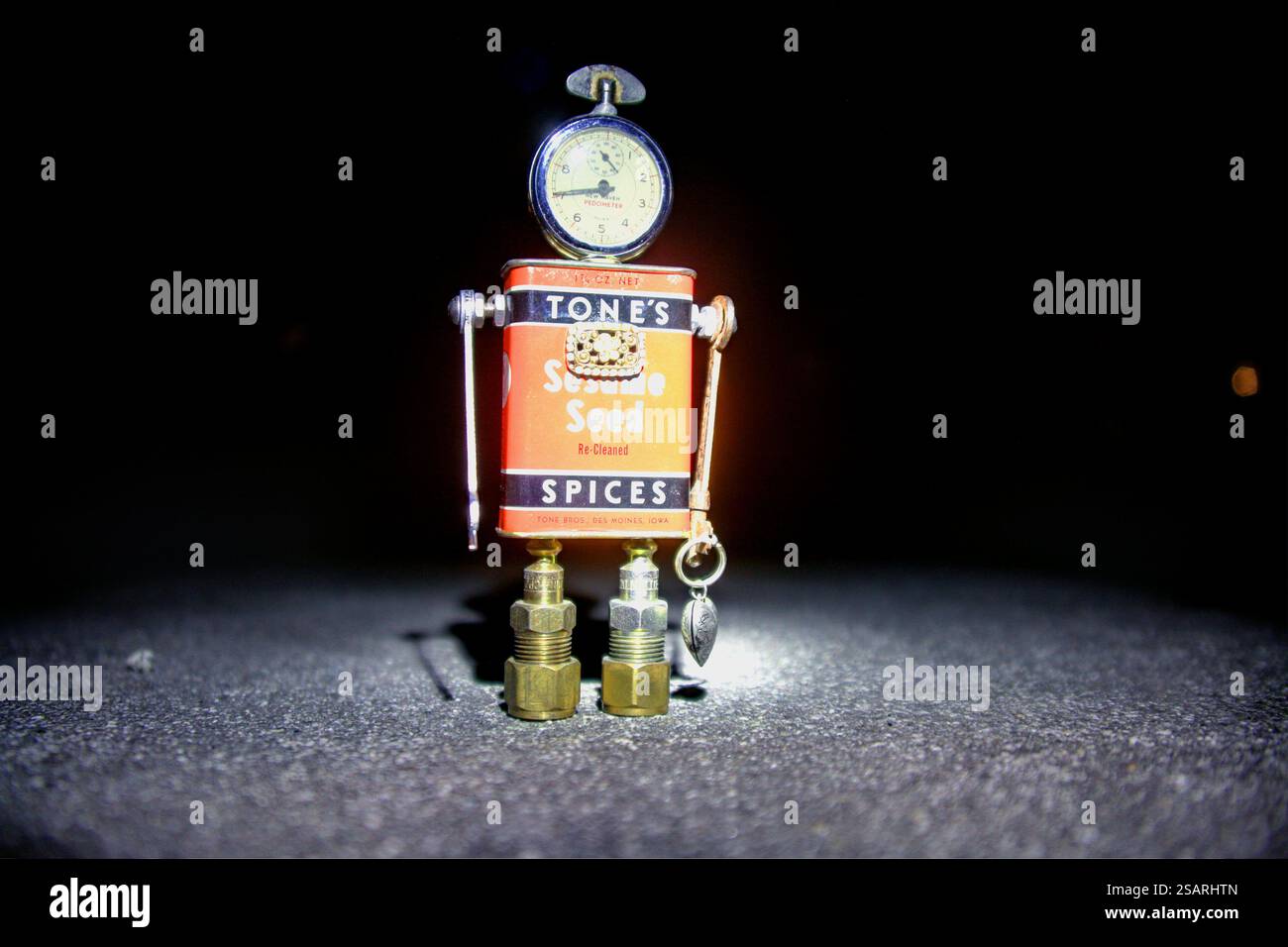 Stravagante scultura robotica realizzata con stagno di spezie di Tone vintage, raccordi in metallo e una testa del manometro, illuminata creativamente su uno sfondo scuro. Foto Stock