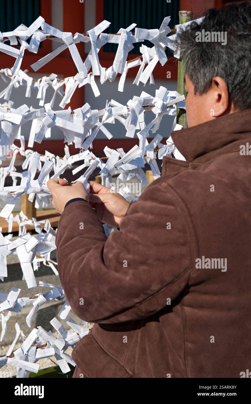 Persone che legano il loro "omikuji" (oracolo di carta di buona o cattiva sorte) a una stringa durante la "Hatsumode" (visita al santuario di Capodanno) a Heian Jingu a Kyoto, Giappone. Foto Stock