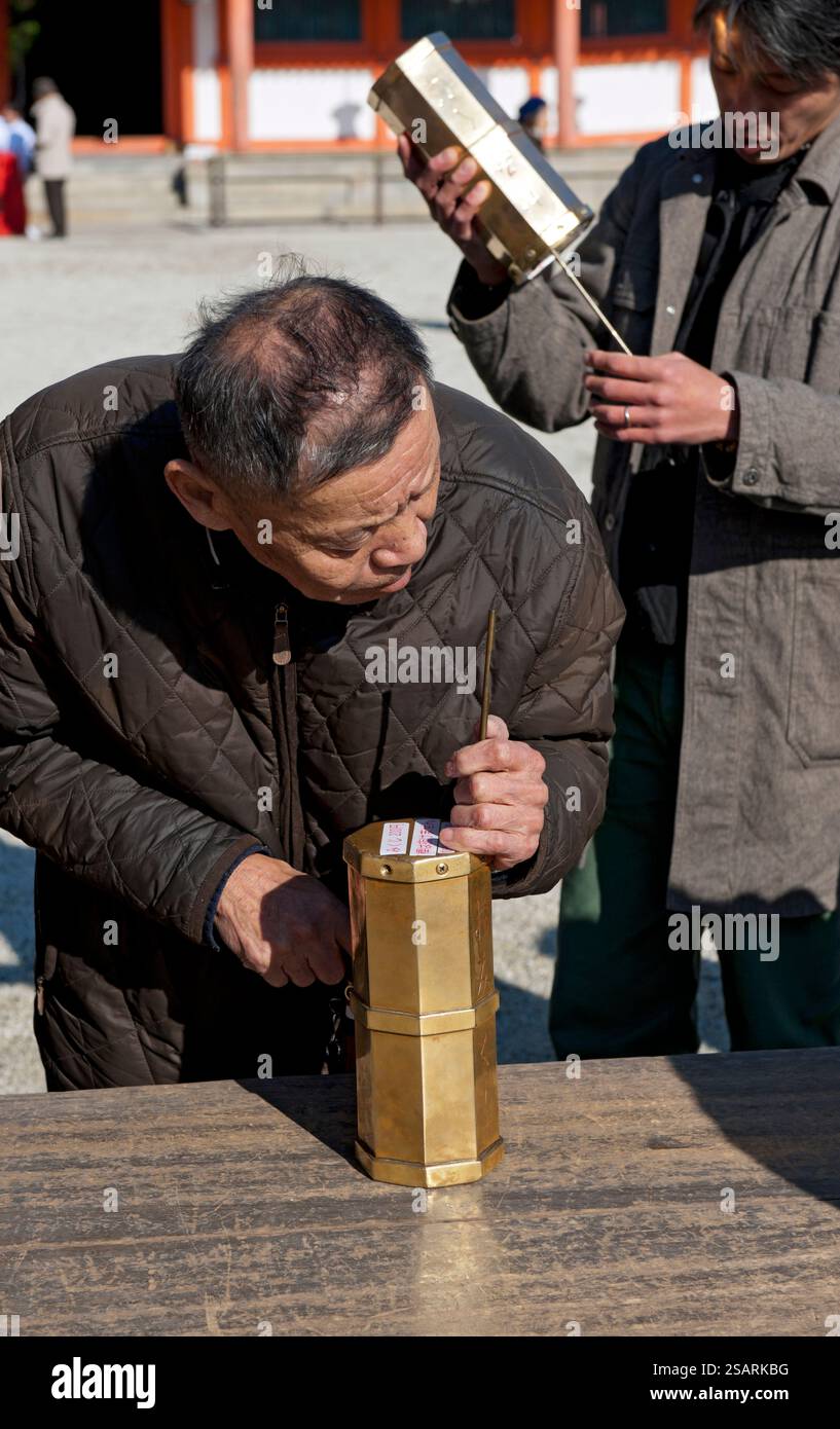 Persone che selezionano un numero da una tanica metallica "omikuji" (oracolo) durante la "Hatsumode" (visita al santuario di Capodanno) augurando buona fortuna a Heian Jingu. Foto Stock