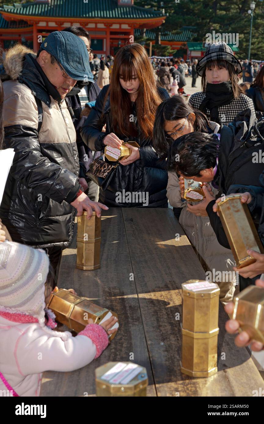 Persone che selezionano un numero da una tanica metallica "omikuji" (oracolo) durante la "Hatsumode" (visita al santuario di Capodanno) augurando buona fortuna a Heian Jingu. Foto Stock