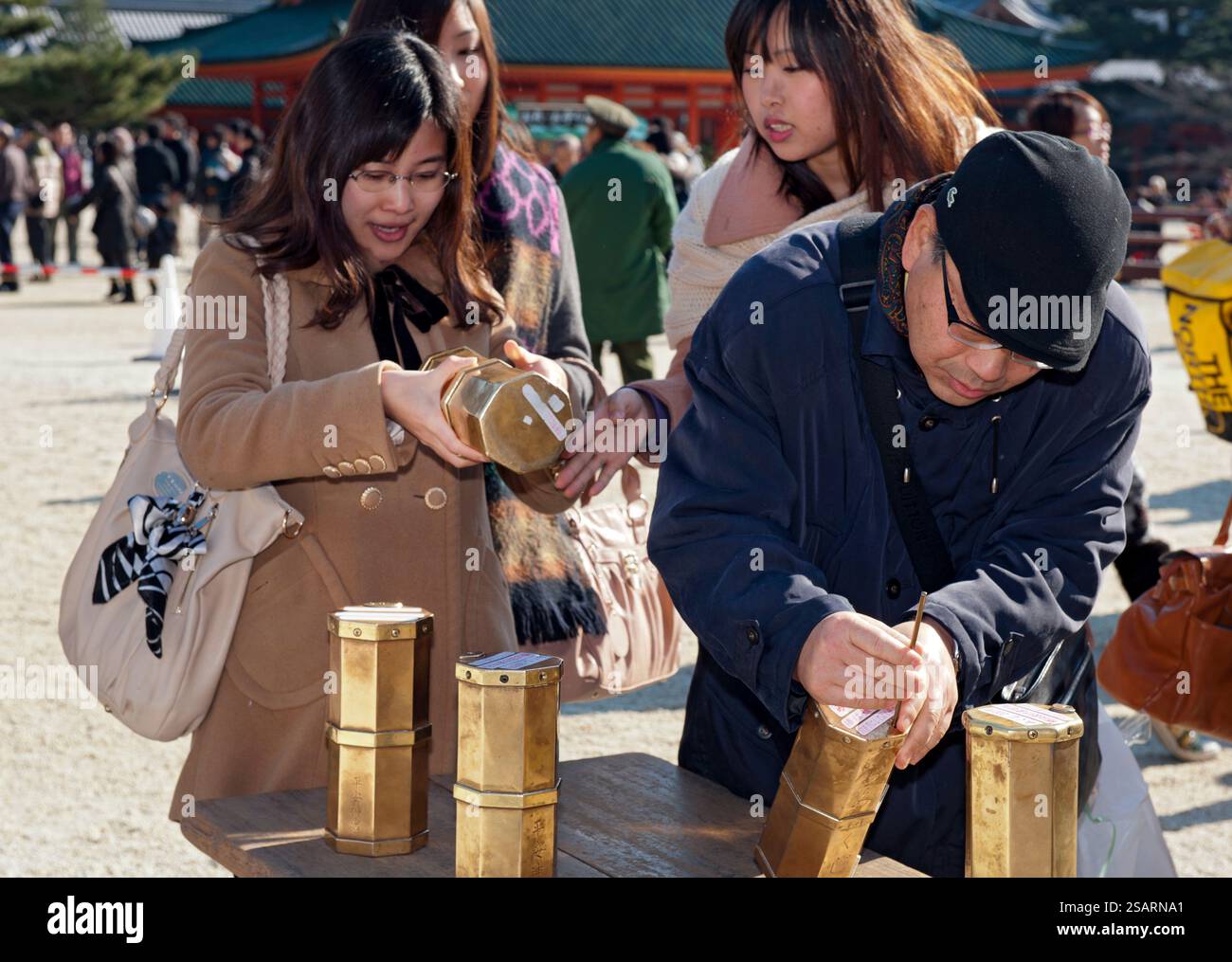 Persone che selezionano un numero da una tanica metallica "omikuji" (oracolo) durante la "Hatsumode" (visita al santuario di Capodanno) augurando buona fortuna a Heian Jingu. Foto Stock