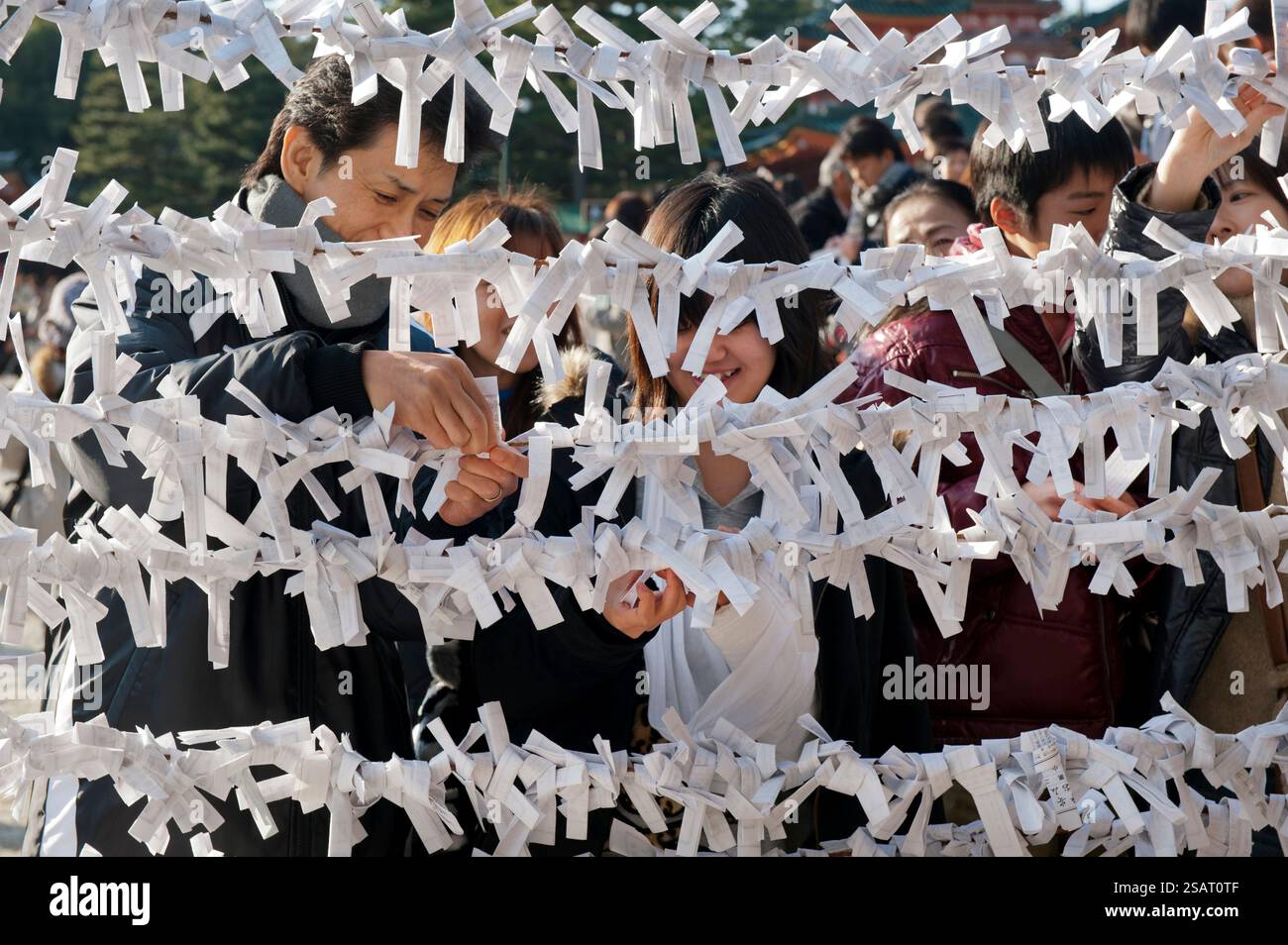 Persone che legano il loro "omikuji" (oracolo di carta di buona o cattiva sorte) a una stringa durante la "Hatsumode" (visita al santuario di Capodanno) a Heian Jingu a Kyoto, Giappone. Foto Stock