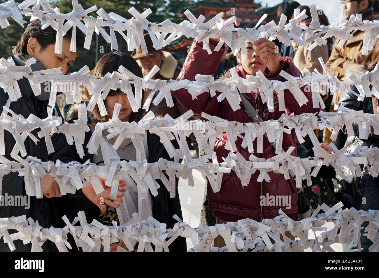Persone che legano il loro "omikuji" (oracolo di carta di buona o cattiva sorte) a una stringa durante la "Hatsumode" (visita al santuario di Capodanno) a Heian Jingu a Kyoto, Giappone. Foto Stock