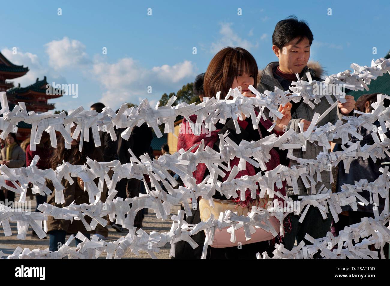 Persone che legano il loro "omikuji" (oracolo di carta di buona o cattiva sorte) a una stringa durante la "Hatsumode" (visita al santuario di Capodanno) a Heian Jingu a Kyoto, Giappone. Foto Stock