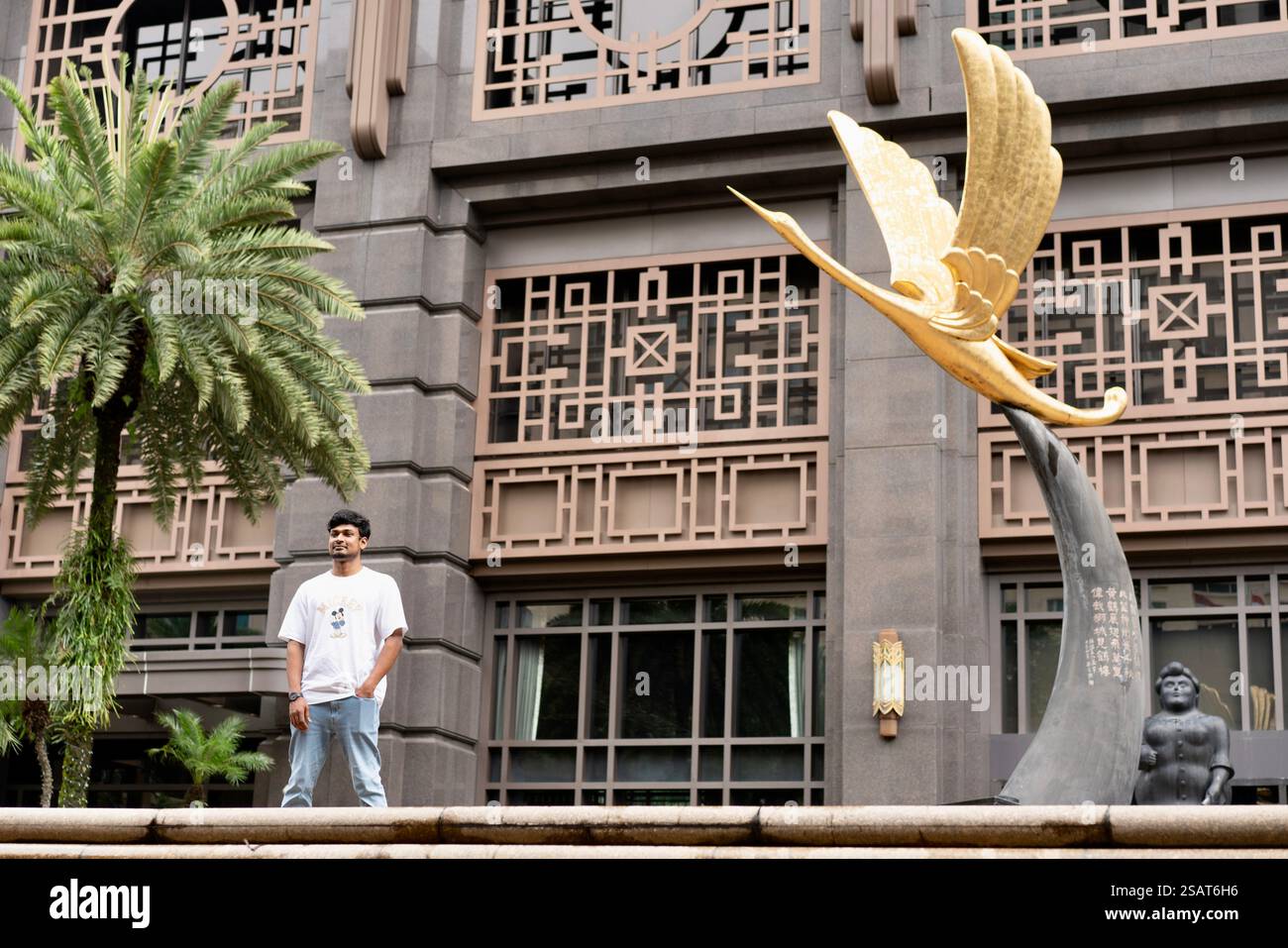 L'uomo di 30 anni stava tranquillamente accanto alla statua di uccello intemprata, il suo sguardo lontano, perso nel pensiero. La luce serale proietta lunghe ombre Foto Stock
