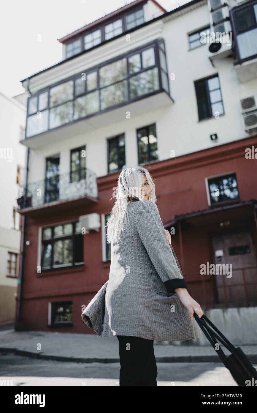 Una donna con un blazer grigio cammina elegantemente di fronte all'architettura urbana Foto Stock