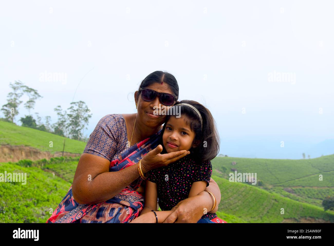 Questa immagine mostra una scena emozionante di una nonna indiana e sua figlia in una piantagione di tè durante la mattina. Foto Stock