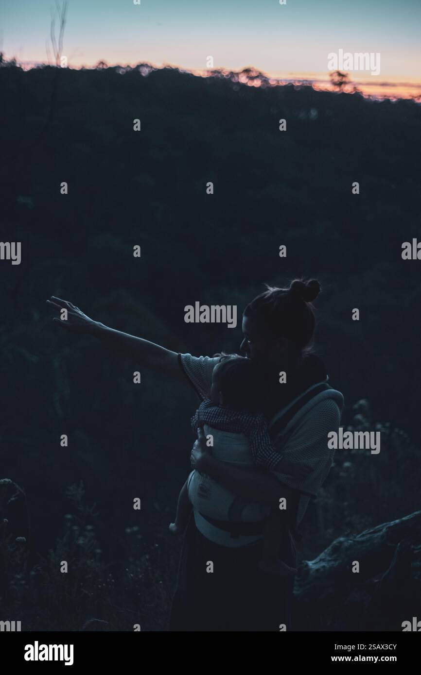 madre punta a vedere con il bambino in braccio al crepuscolo in natura Foto Stock