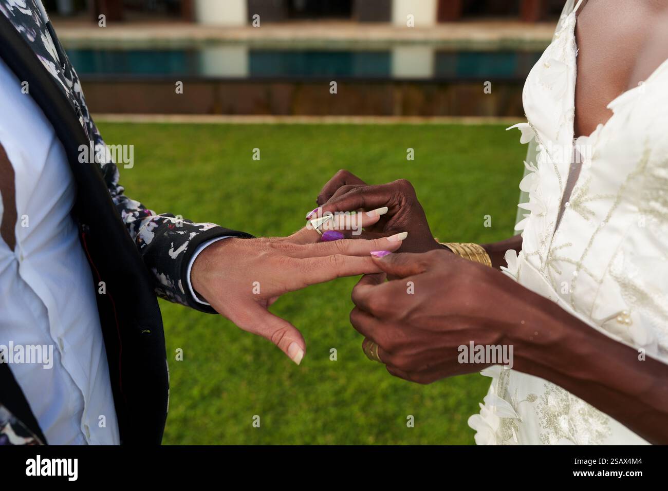 Coppia fluida di genere ambigua in abito bianco, audaci anelli per lo scambio di abiti alla villa tropicale. Fresco ambiente per matrimoni lgbtq. L'eleganza della sposa incontra lo sposo Foto Stock
