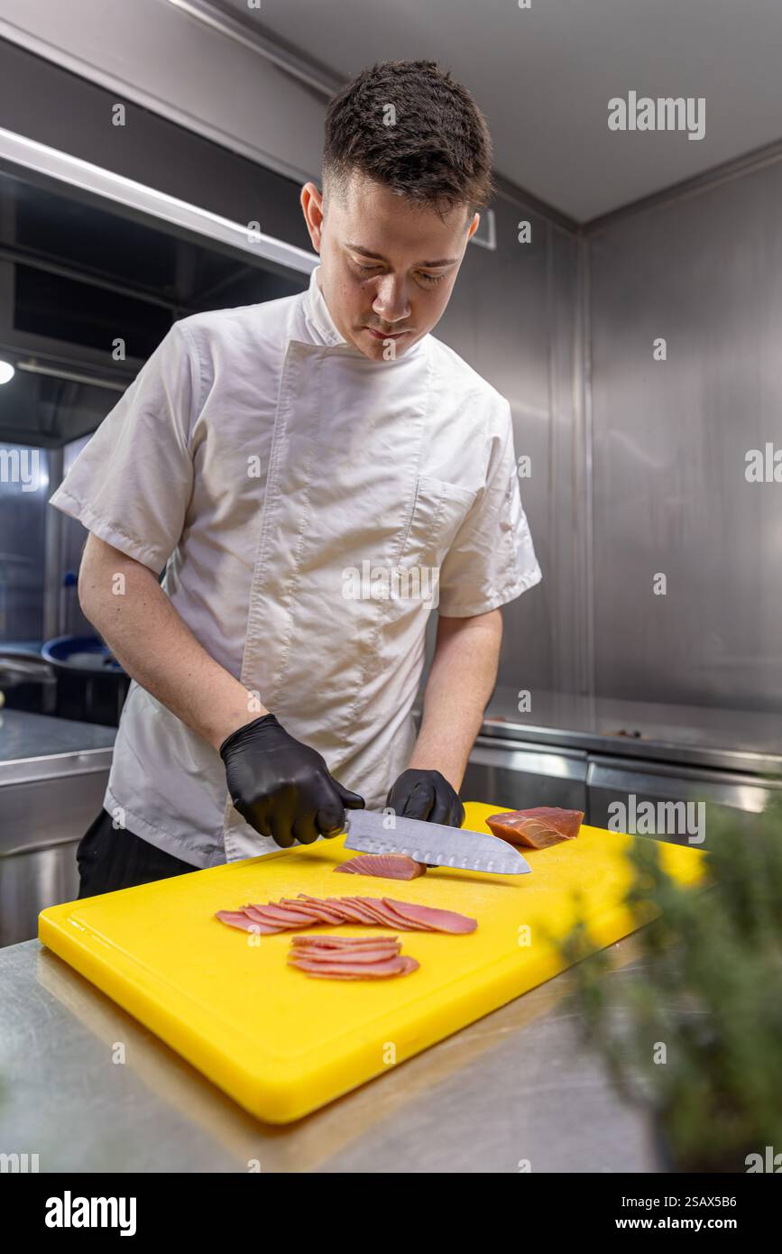 Lo chef affetta la carne su un tagliere giallo nella cucina moderna Foto Stock