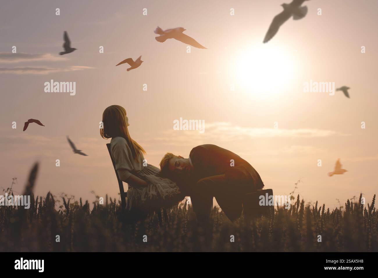 Una coppia avvolta dalla luce del tramonto scambia gesti d'amore in un campo Foto Stock