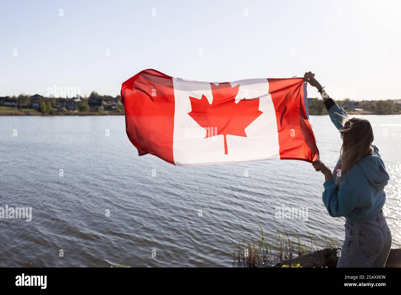 Donna che regge una bandiera canadese sullo sfondo del cielo, del sole e del fiume. Viaggi, immigrazione. Buon Canada Day. Orgoglio, libertà, simbolo nazionale Foto Stock