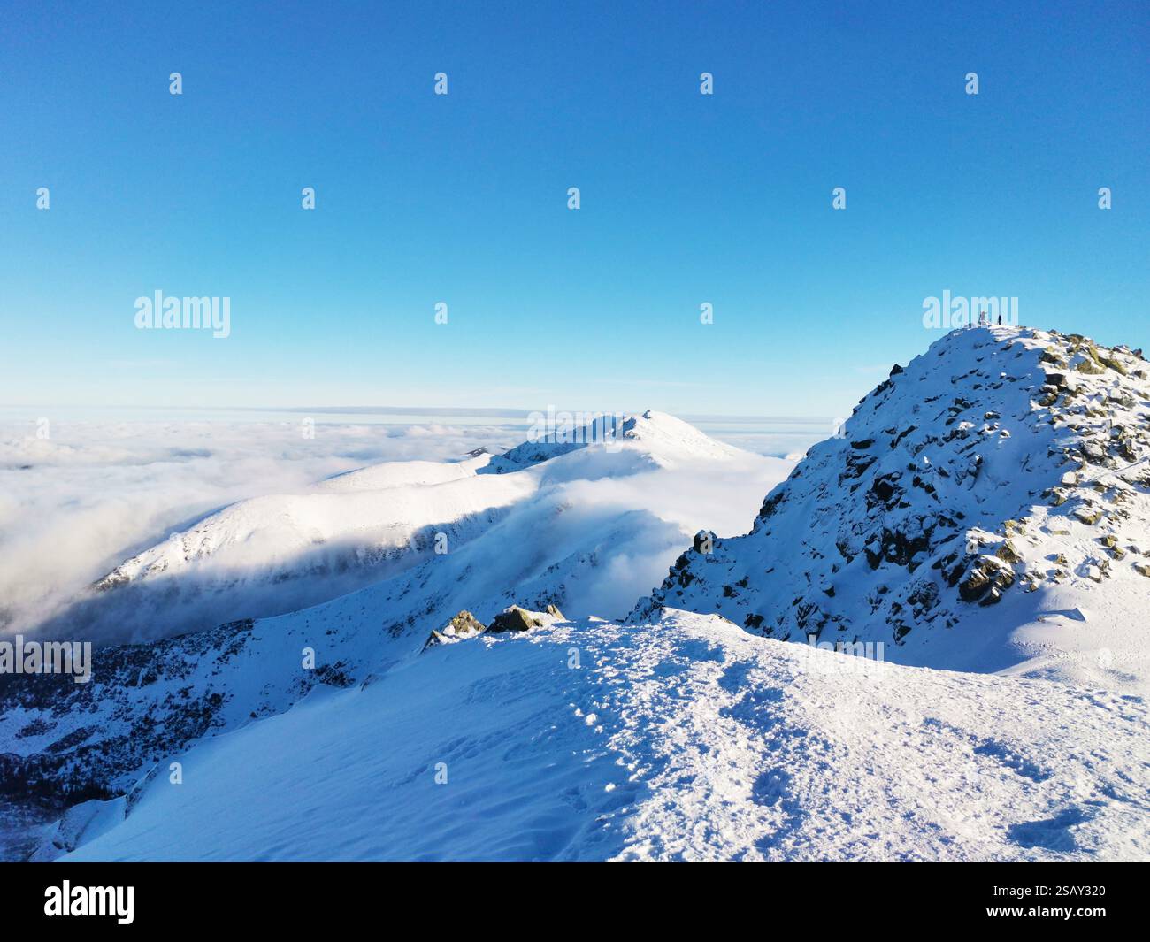 Vetta della montagna coperta di neve circondata da nuvole. Vista dall'alto. Giornate invernali soleggiate e limpide. Gente in cima alla montagna Foto Stock