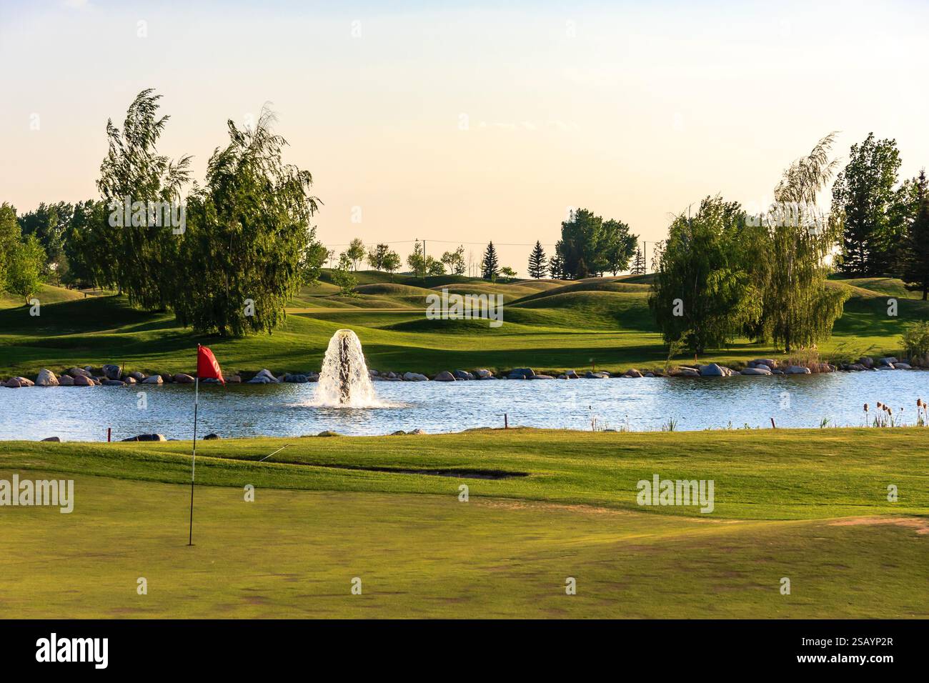 Campo da golf con laghetto e bandiera rossa a terra. Lo stagno è circondato da alberi e l'erba è verde Foto Stock