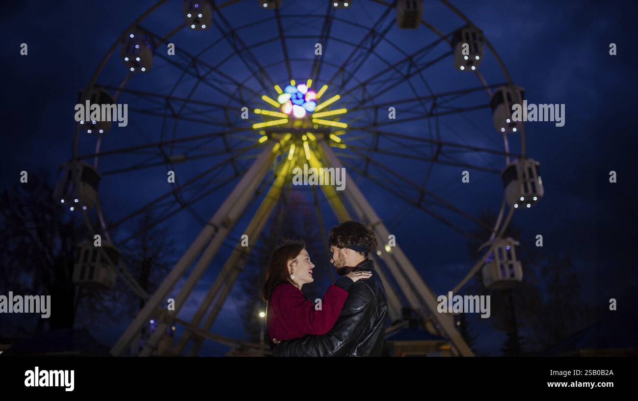 Coppia in piedi sotto una ruota panoramica illuminata di notte Foto Stock