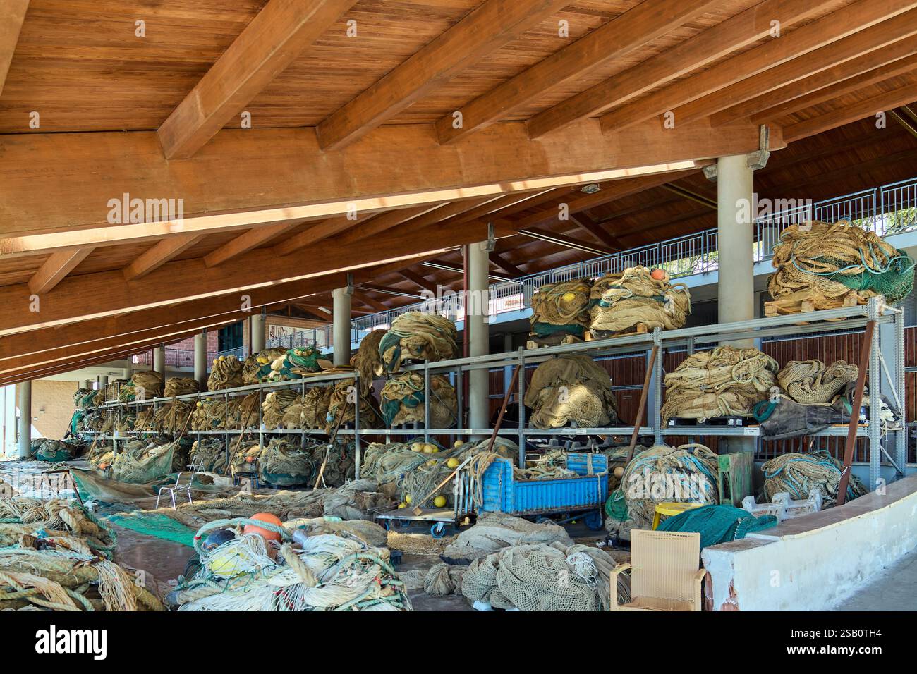 Uno spazio di lavoro rustico per la manutenzione delle reti da pesca con funi, reti e boe sotto una struttura in legno. Una parte vitale del lavoro quotidiano dell'industria della pesca. Foto Stock