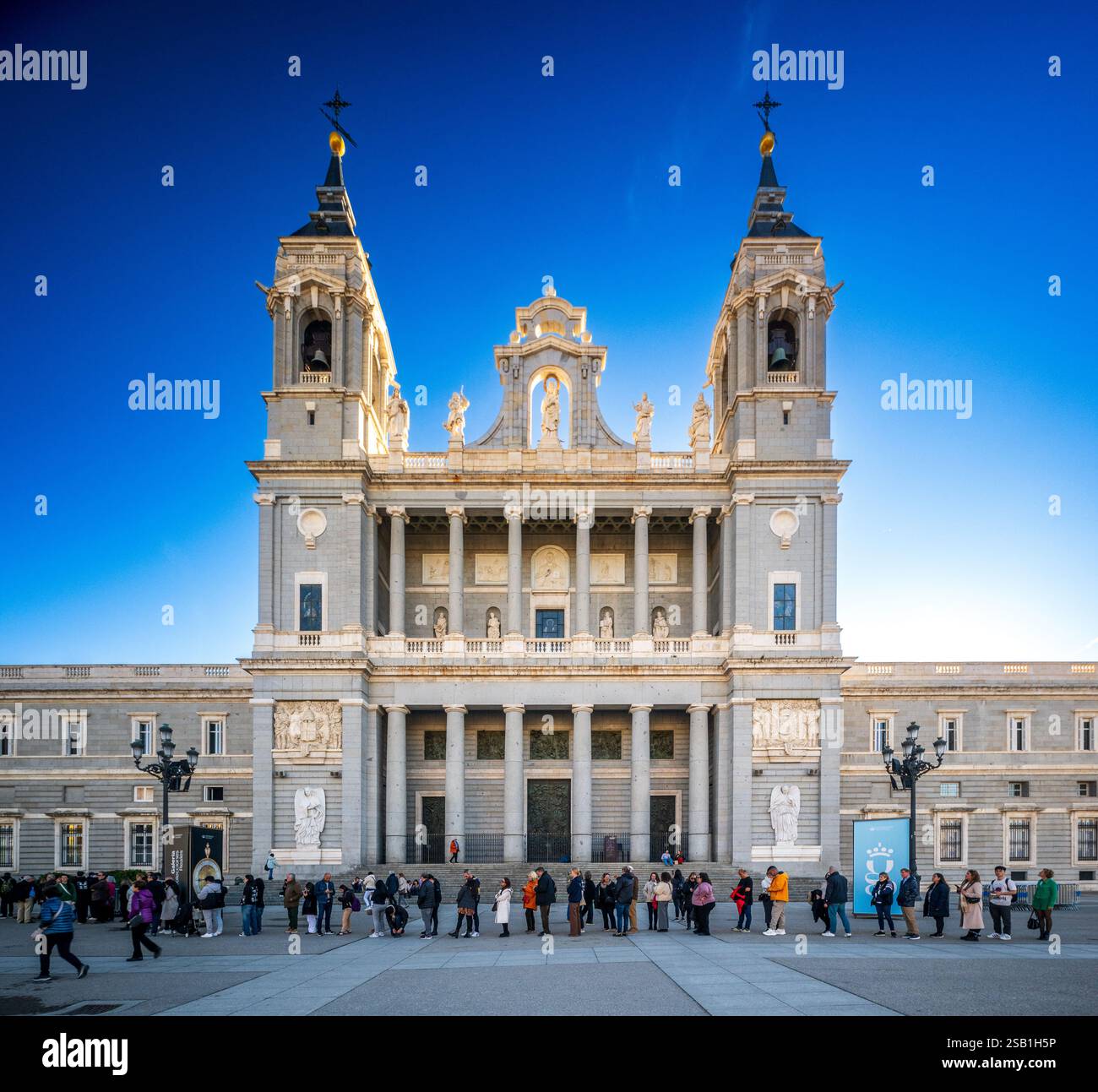 Vista frontale della facciata della Cattedrale di Almudena sotto il cielo limpido con una folla a Madrid. Foto Stock