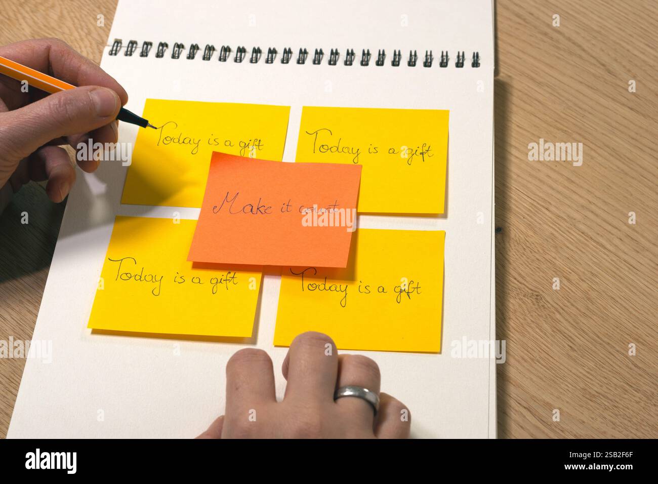 Una persona sta scrivendo su un taccuino con rilegatura a spirale. All'interno del notebook è presente una nota adesiva gialla che dice "oggi è un regalo, fallo contare" Foto Stock