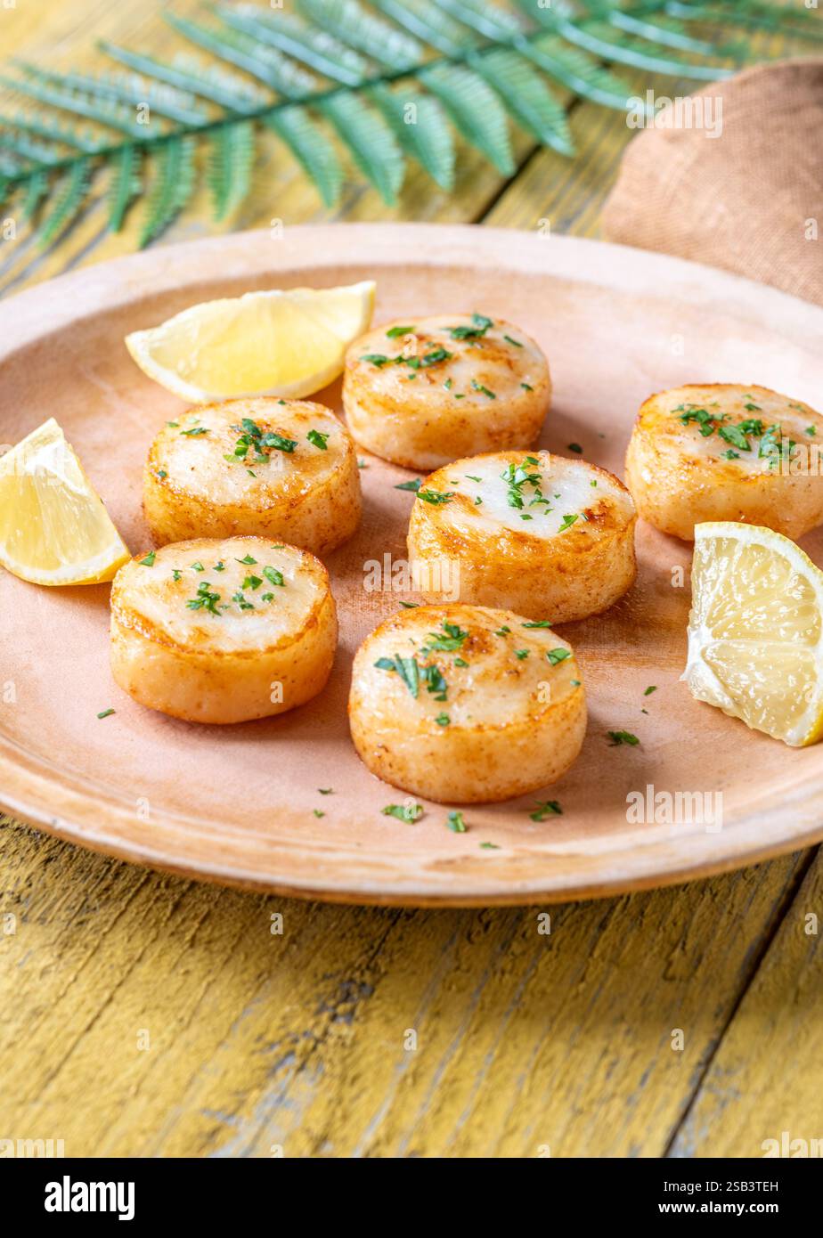 Morbide capesante fritte in burro servite con limone, prezzemolo, rustico fondo giallo Foto Stock