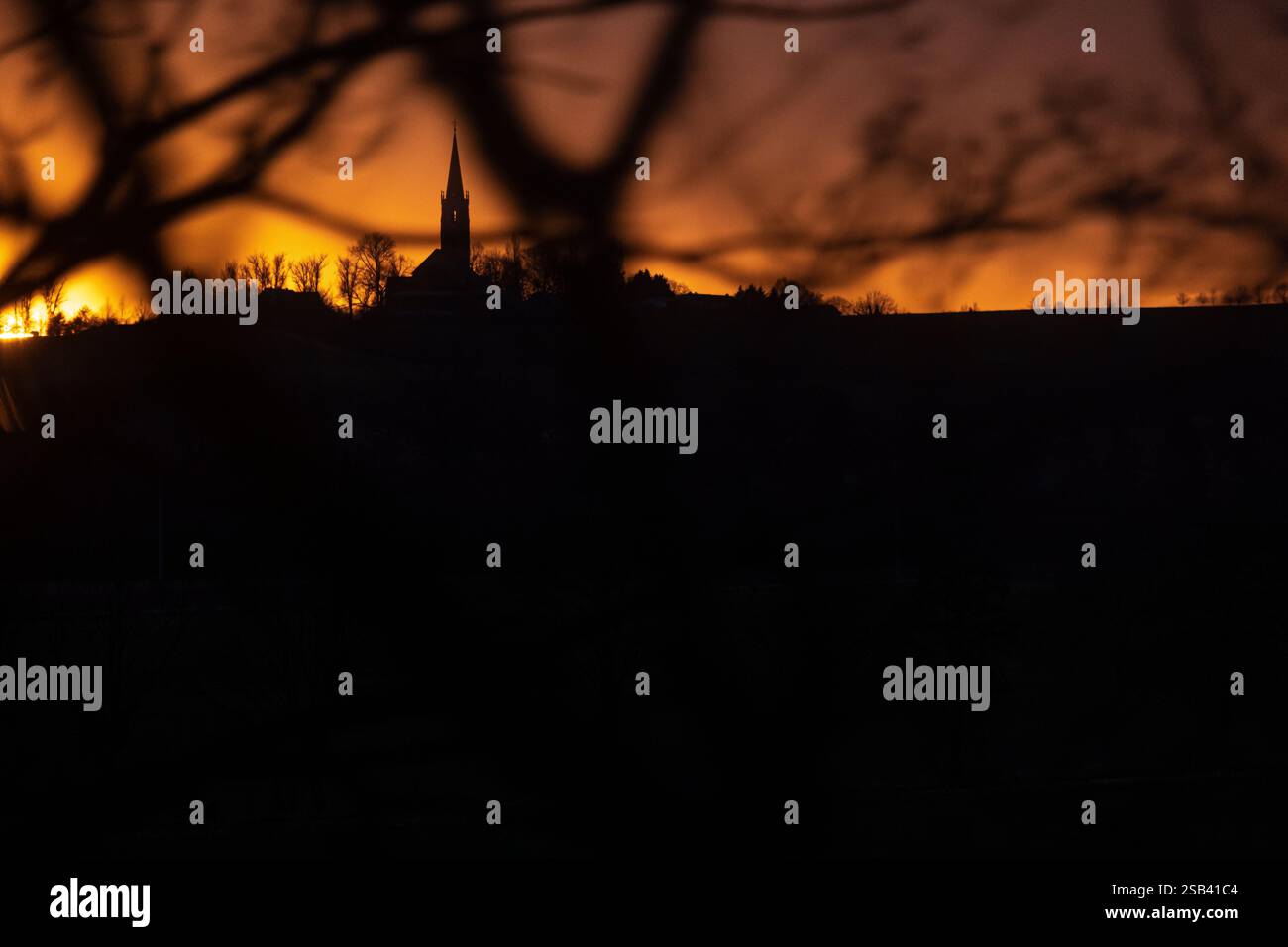 Una chiesa rurale tedesca al tramonto vista attraverso i rami degli alberi in inverno Foto Stock