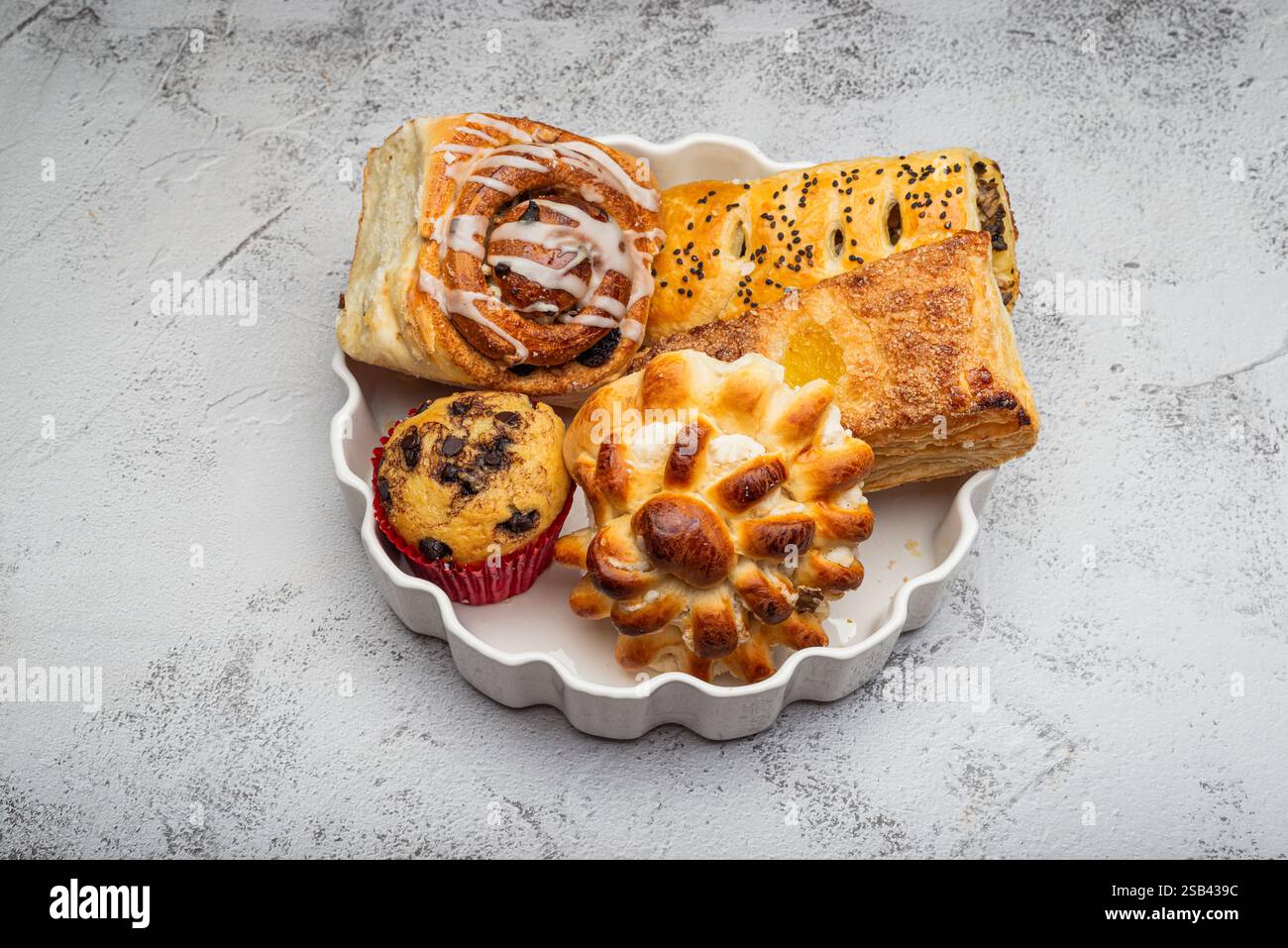 Primo piano di un piatto bianco con diversi dessert appena sfornati, dolci alla cannella, cupcake e un dolce dolce. Foto Stock