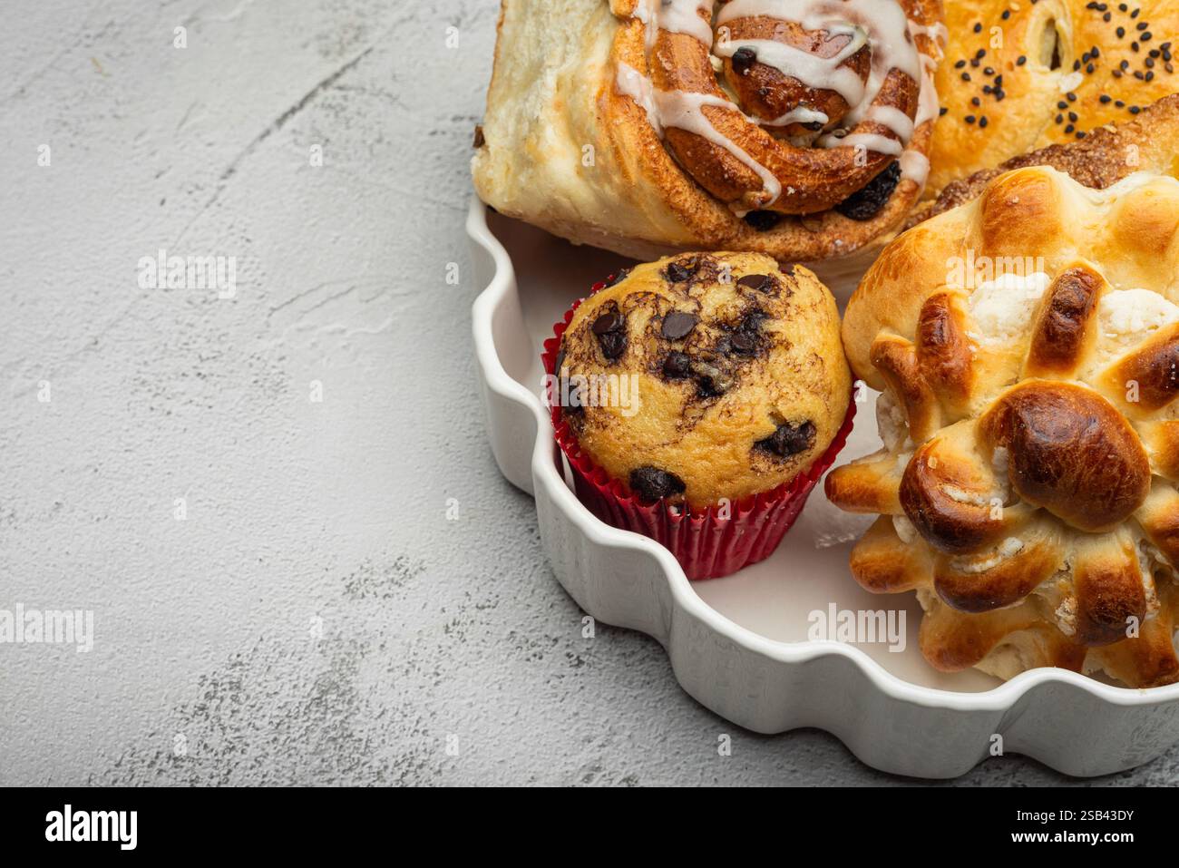 Primo piano di un piatto bianco con diversi dessert appena sfornati, dolci alla cannella, cupcake e un dolce dolce. Foto Stock