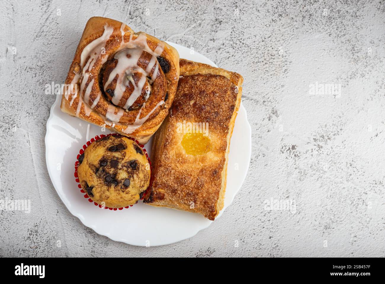 Primo piano di un piatto bianco con diversi dessert appena sfornati, dolci alla cannella, cupcake e un dolce dolce. Foto Stock