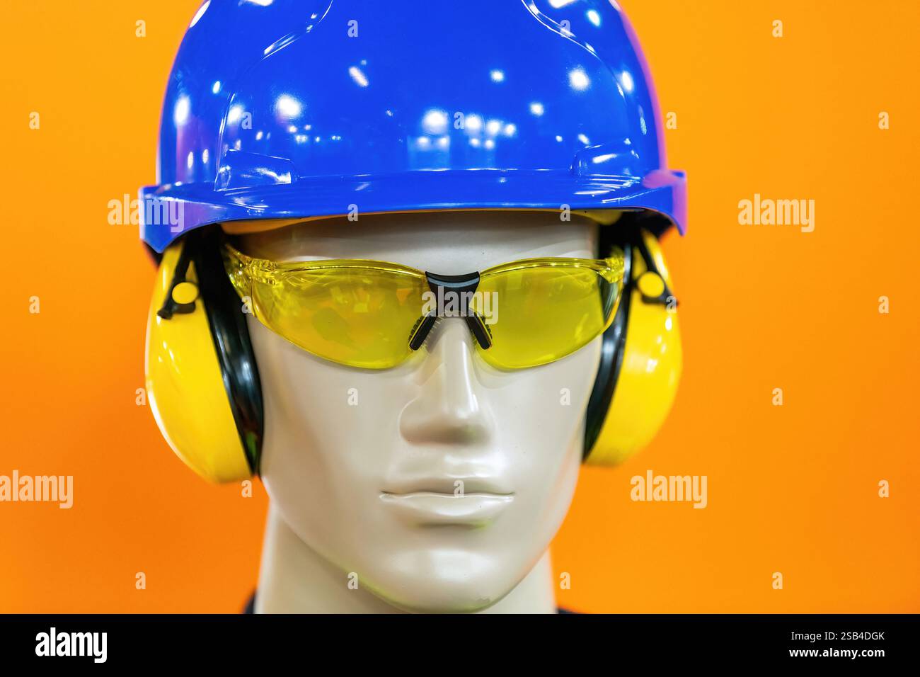 Manichino con dispositivi di protezione individuale (DPI) dotati di equipaggiamento di sicurezza essenziale, tra cui un elmetto blu, protezioni gialle per le orecchie e occhiali di sicurezza colorati. Ideale per la presentazione di attrezzature per la costruzione o la sicurezza industriale. Foto Stock
