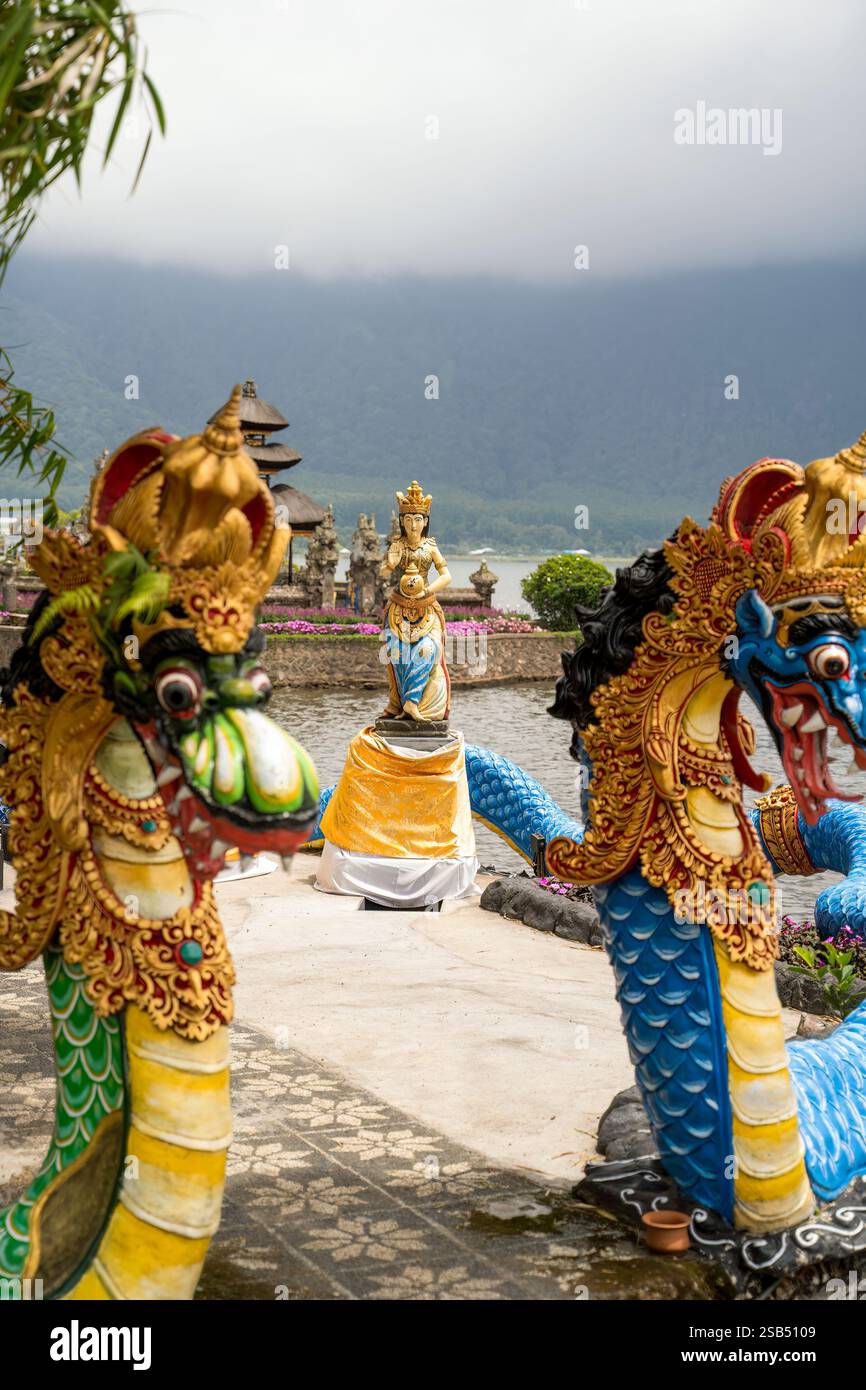Dettagliate sculture di draghi incorniciano una statua serena e il paesaggio nebbioso del lago Batur a Bali. Una fusione di elementi culturali e bellezze naturali crea un Foto Stock