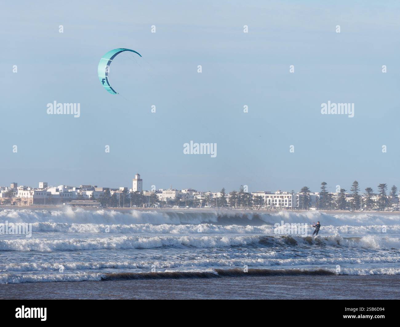 Kite surfer tra le onde con la storica Medina alle spalle nella città di Essaouira, 27-29 gennaio 2025 Foto Stock