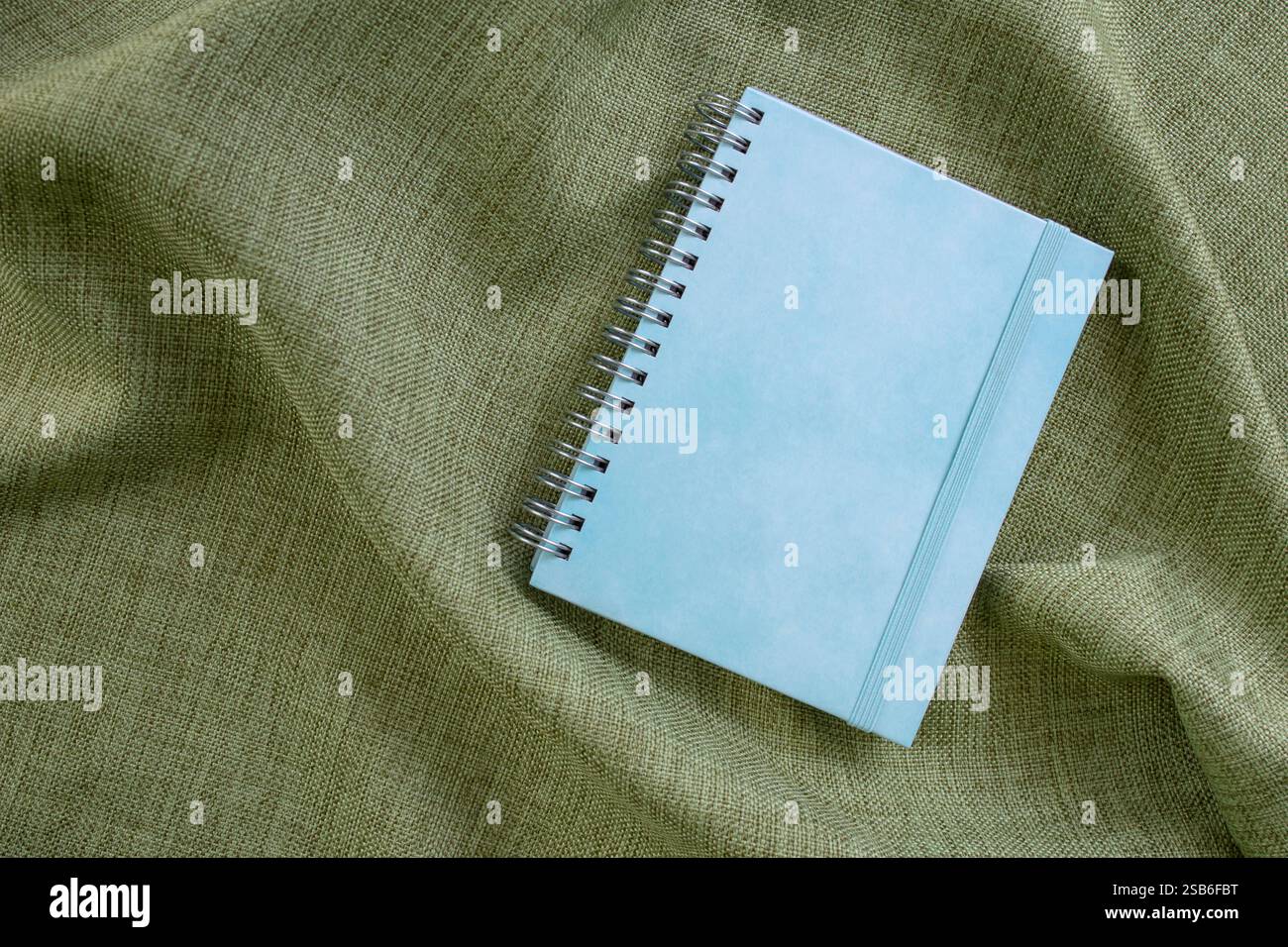Notebook con copertina rigida blu vuoto su sfondo in tessuto verde oliva, spazio di copia per il testo Foto Stock