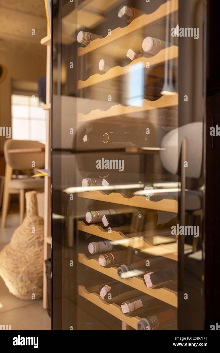 Un elegante refrigeratore per vini con porta in vetro trasparente che presenta un'elegante collezione di bottiglie di vino, perfettamente posizionato in un moderno ambiente ristorante. Foto Stock