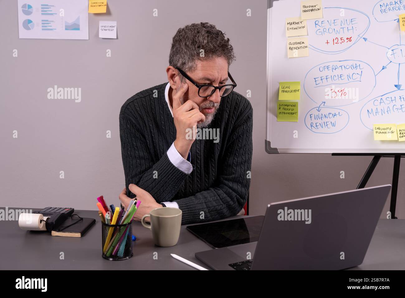 Business manager che analizza in modo approfondito i dati finanziari alla scrivania dell'ufficio, rappresentando il pensiero strategico e la pianificazione aziendale. Foto Stock