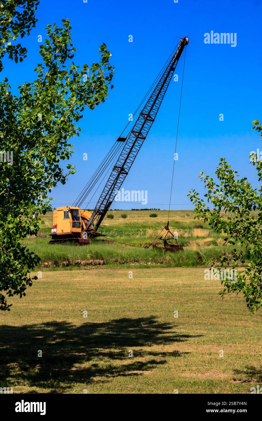 Una grande gru è seduta in un campo con alberi sullo sfondo. La gru è vecchia e arrugginita, ed è abbandonata. La scena ha un senso di solitudine Foto Stock