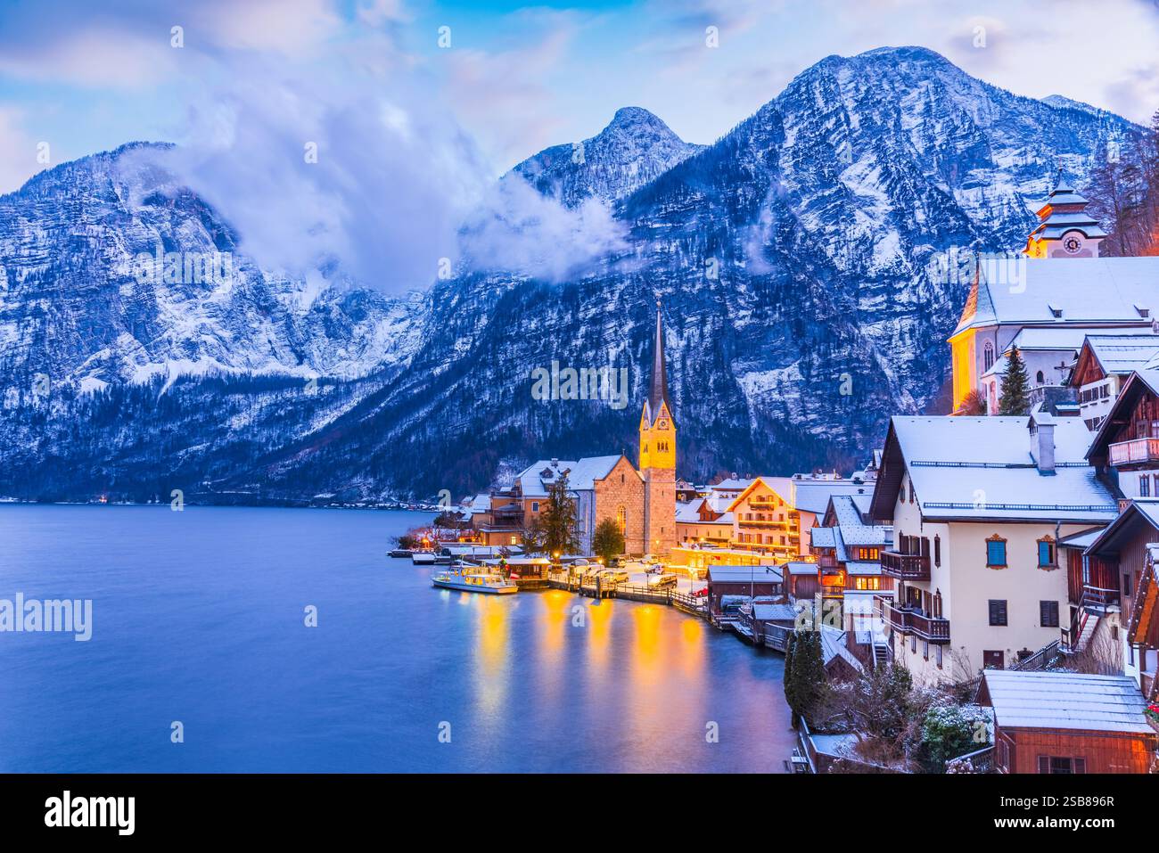 Hallstatt, Austria. Tranquillo villaggio alpino con un lago tranquillo, tetti innevati e uno sfondo mozzafiato durante il crepuscolo invernale. Foto Stock