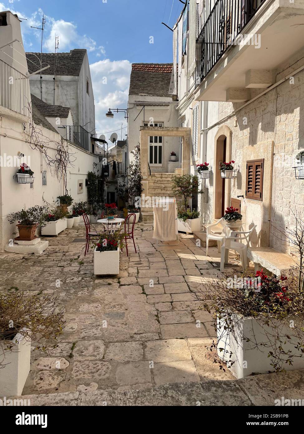 Pittoresco cortile con piccola area salotto e piante in vaso nel centro storico di noci, Italia - Immagine stock catturata con smartphone