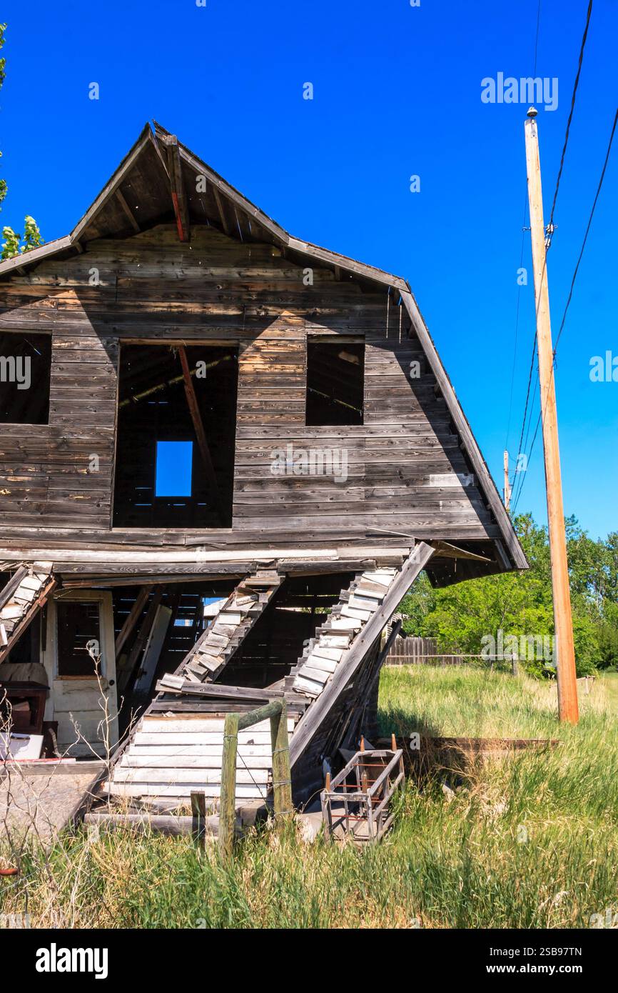 Un vecchio fienile fatizzato con un palo sporgente dal terreno. Il fienile è in un campo con erba alta Foto Stock