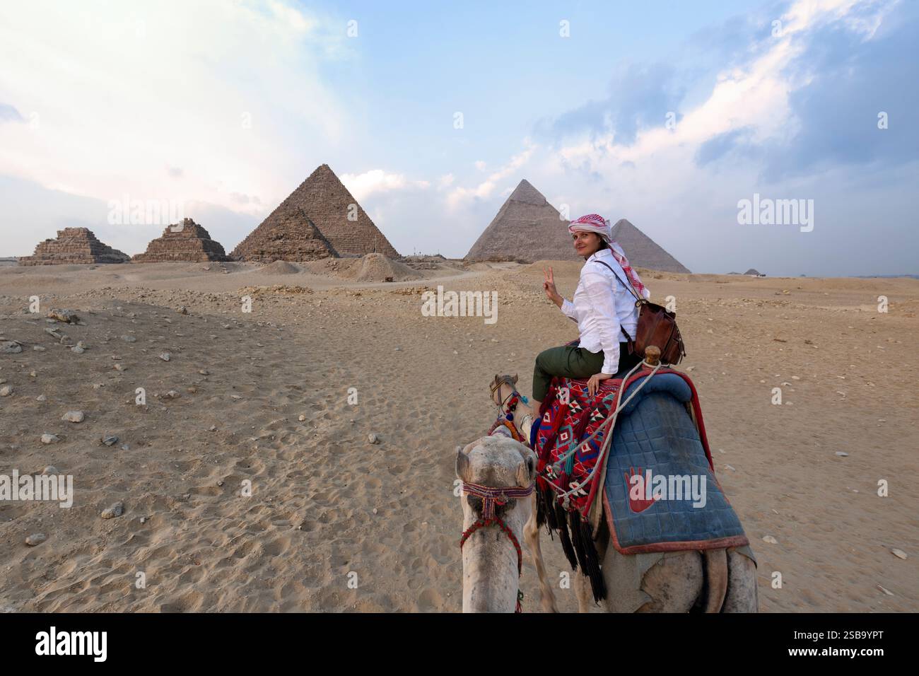 Donna con lunghi capelli scuri montato su un dromedario sulla schiena guardando le piramidi d'Egitto Foto Stock