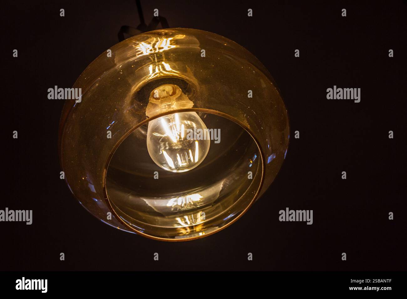 Lampada a pendente moderna in vetro giallo illuminata in un ambiente interno scuro Foto Stock