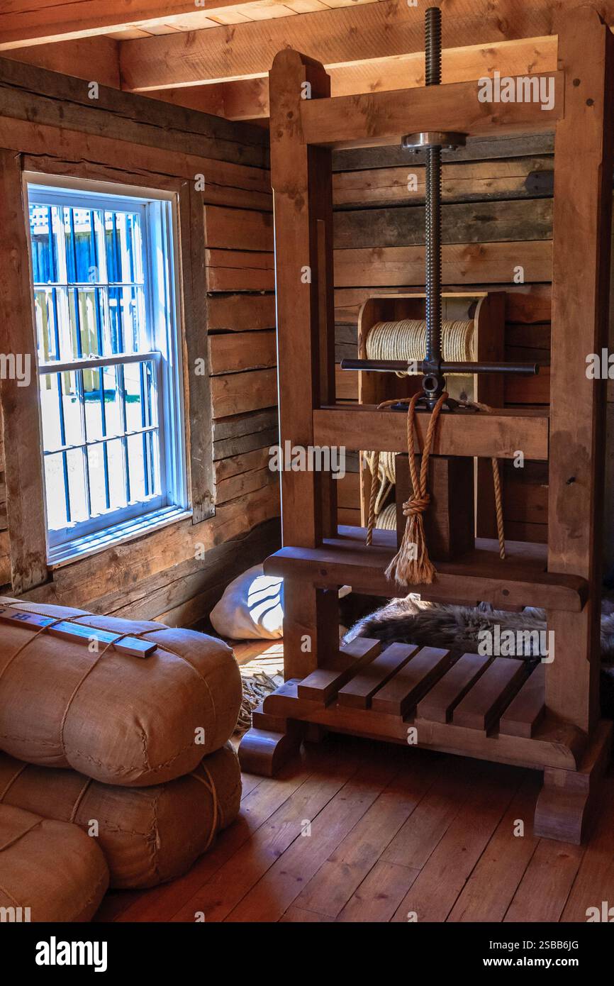 Una pressa in legno e' in una stanza con una finestra. La stampa è vecchia e ha una corda appesa ad essa. La camera è poco illuminata e ha un'atmosfera rustica Foto Stock