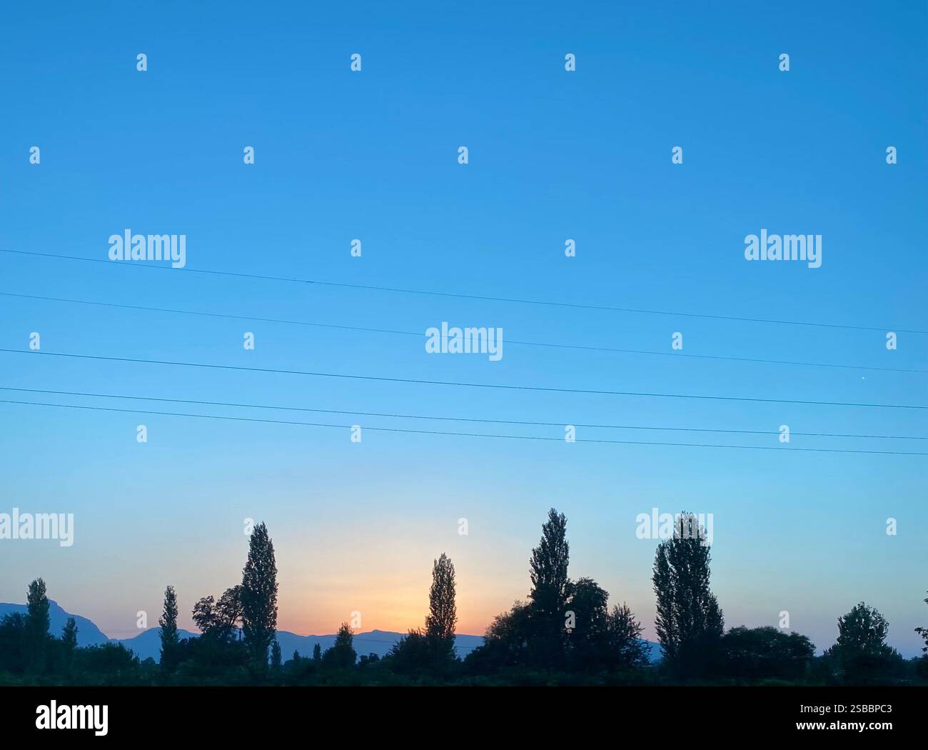 Sfumature arancioni del sole serale che tramonta dietro una montagna creando le sagome degli alberi Foto Stock