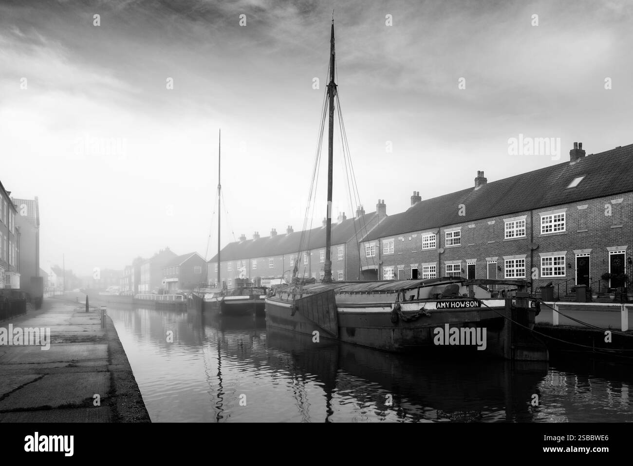 BEVERLEY, Regno Unito - 12 DICEMBRE 2016: Chiatte d'epoca ormeggiate lungo la riva del canale fiancheggiate da case cittadine in una mattina nebbiosa il 12 dicembre 2016. Foto Stock
