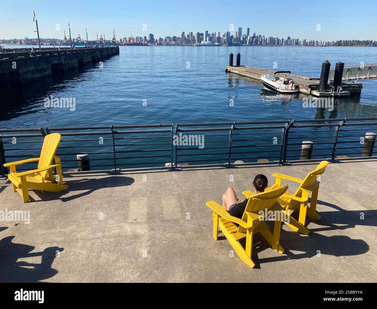 Donna sulla sedia Adirondack che gode della vista sullo skyline di Vancouver dai cantieri navali di North Vancouver, British Columbia, Canada - Immagine stock catturata con smartphone