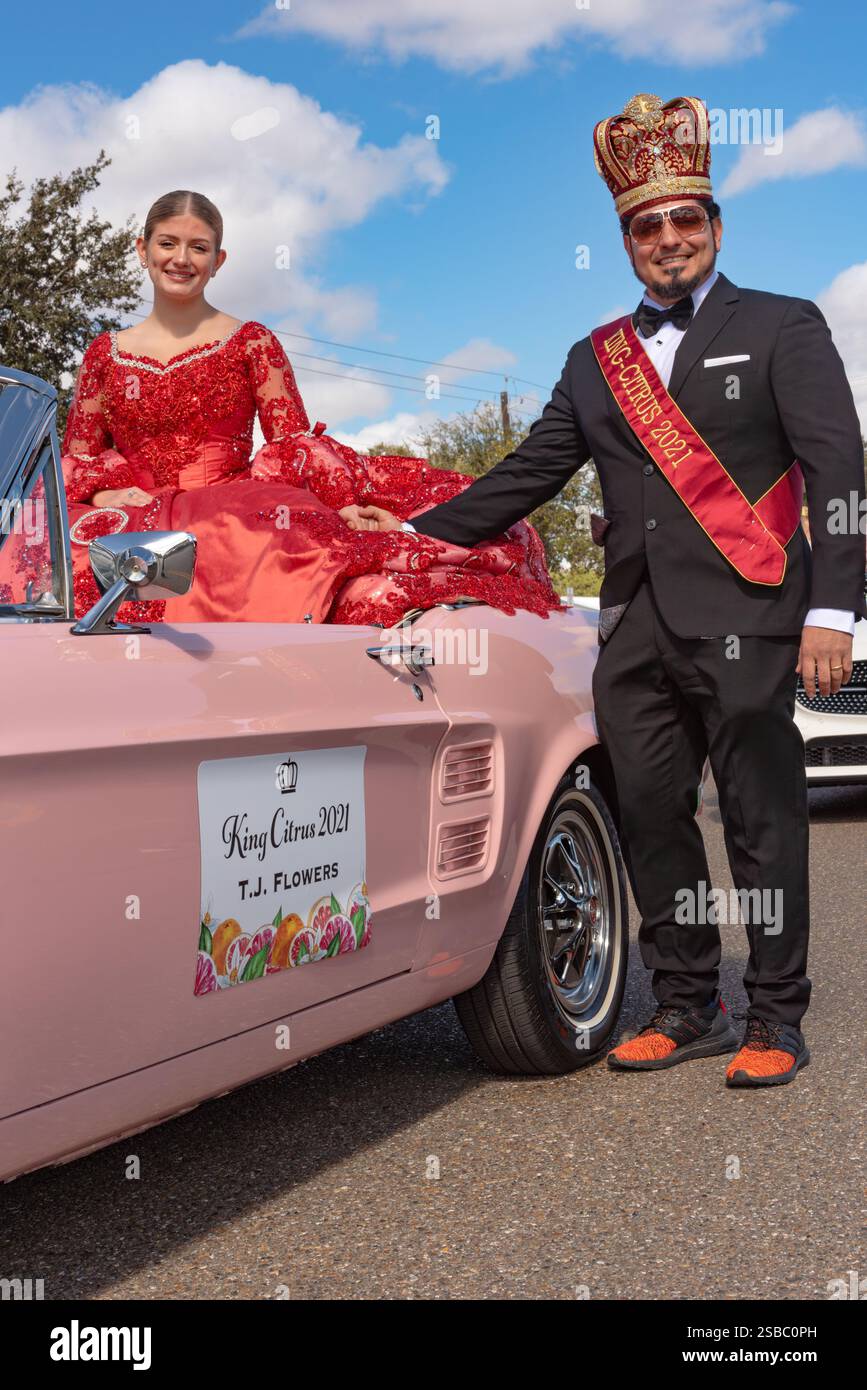 Giovane donna in abito rosso, membro della Queen's Court, in rosa Mustang convertibile e maschio con corona in Parade of Oranges 2025, Mission, Texas, USA. Foto Stock