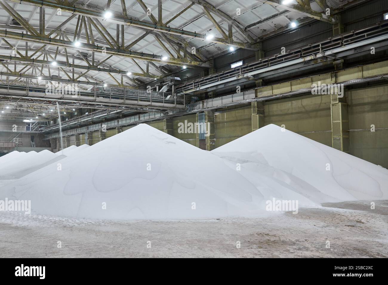 Magazzino di impianti chimici con grandi cumuli di materiale bianco e sistema di trasporto in funzione durante le ore diurne Foto Stock
