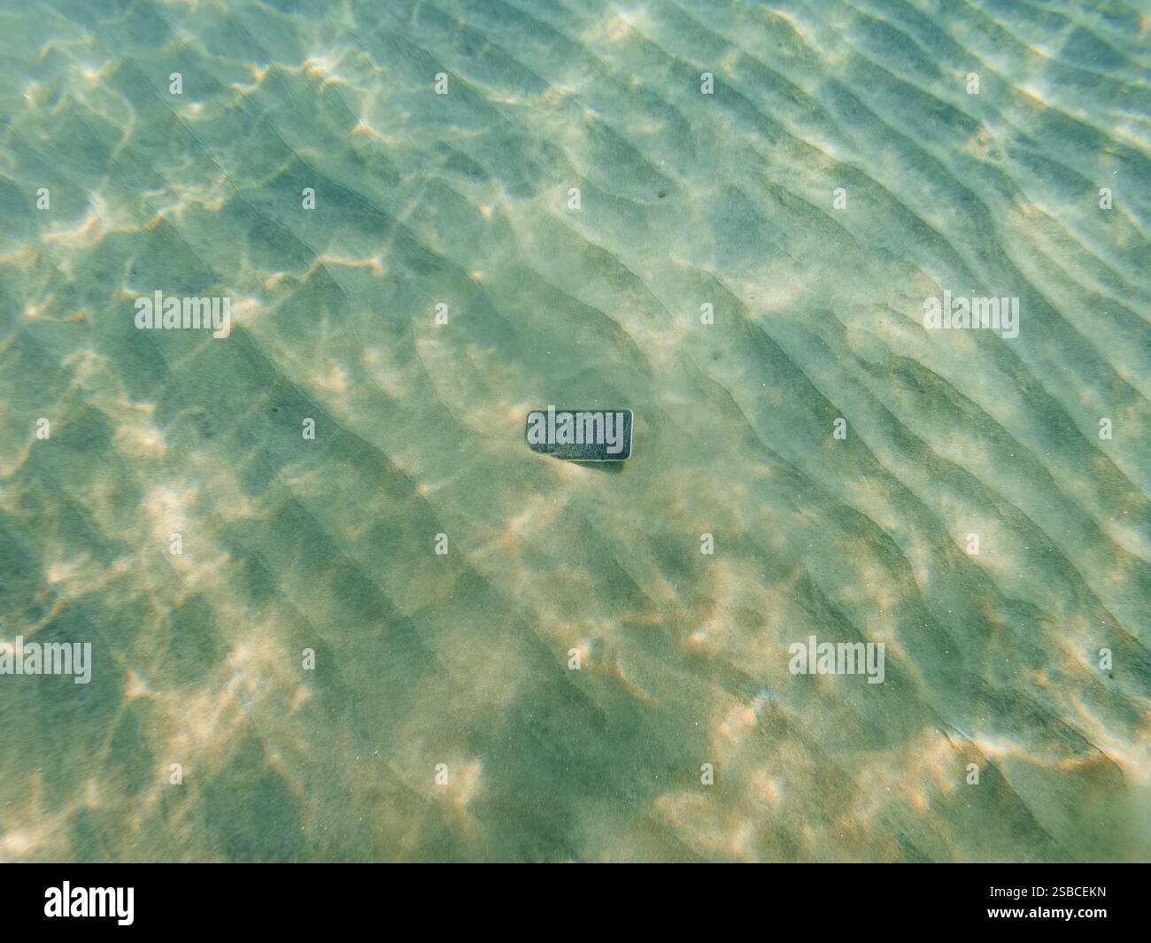 Smarrimento dello smartphone sul fondo dell'oceano nella sabbia, vista ad angolo alto Foto Stock
