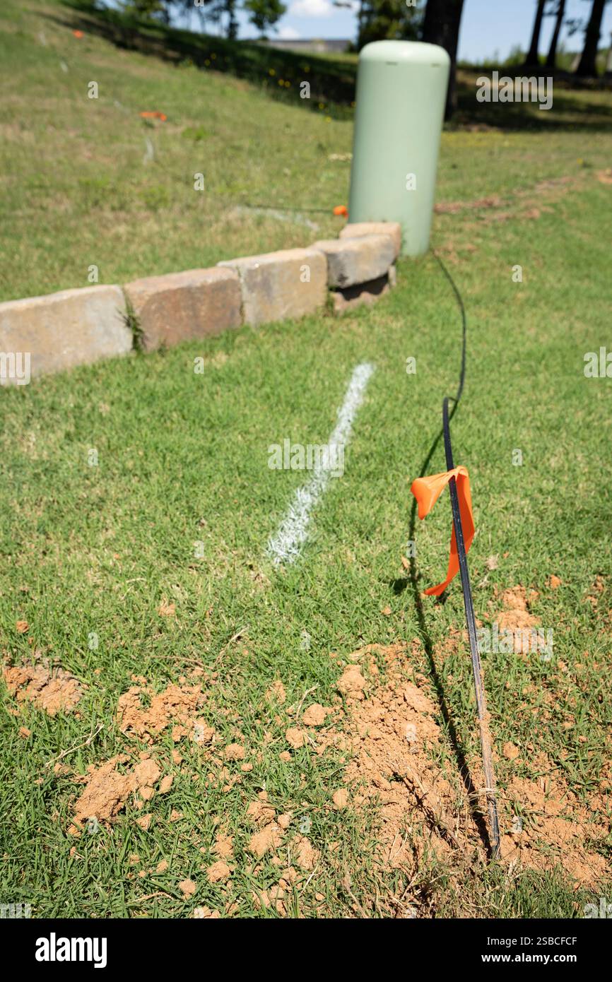 Una profondità di campo ridotta si concentra su una nuova caduta di linea del cavo in fibra ottica sul terreno con un allarme arancione legato intorno ad esso, in attesa di essere sepolto. Foto Stock