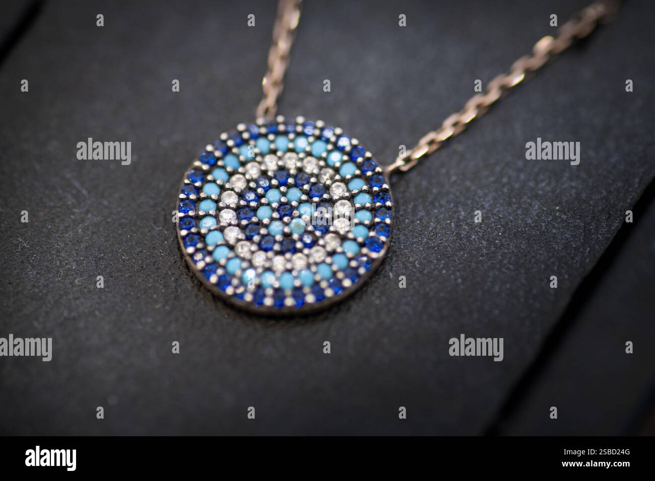 Un primo piano di un ciondolo in argento ispirato al tradizionale design del malocchio, adornato da scintillanti pietre preziose blu e bianche, che simboleggiano la protezione e. Foto Stock